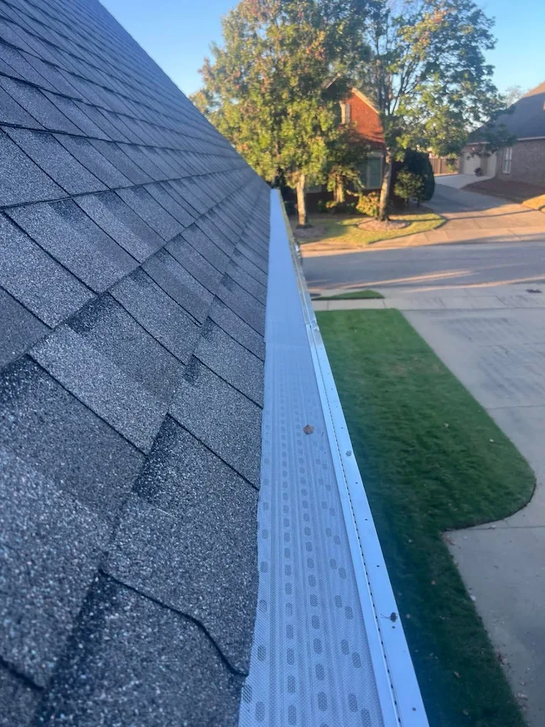 Perforated gutter guard installed along a shingle roof edge